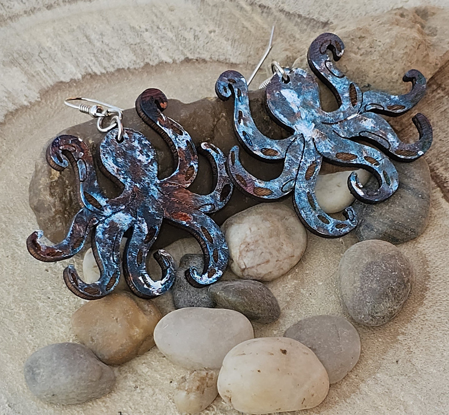 Metallic looking octopus earrings on a stone surface