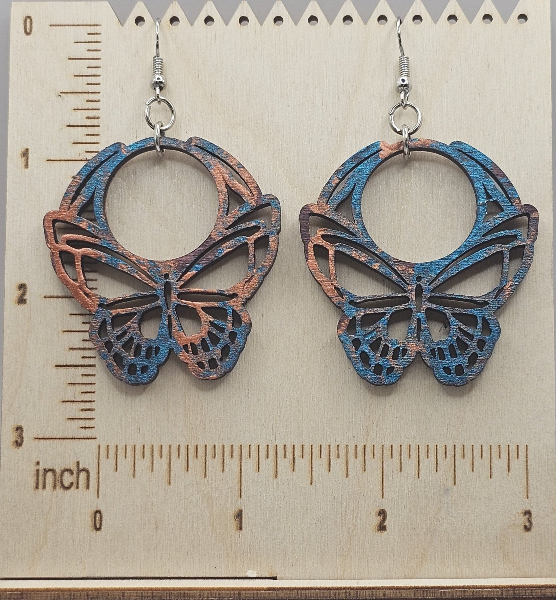 Butterfly-shaped earrings on a wooden surface with a ruler for scale.