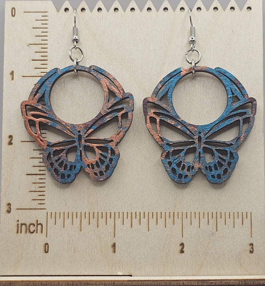 Butterfly-shaped earrings on a wooden surface with a ruler for scale.