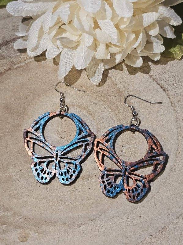 Butterfly-shaped earrings on a textured surface with white flowers in the background