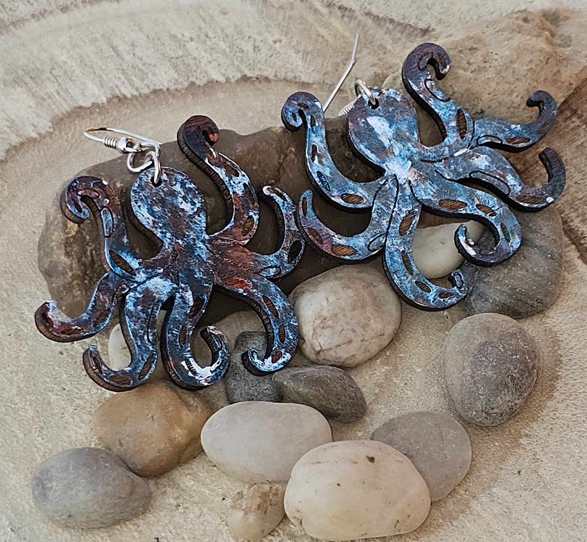 Metallic looking octopus earrings on a stone surface