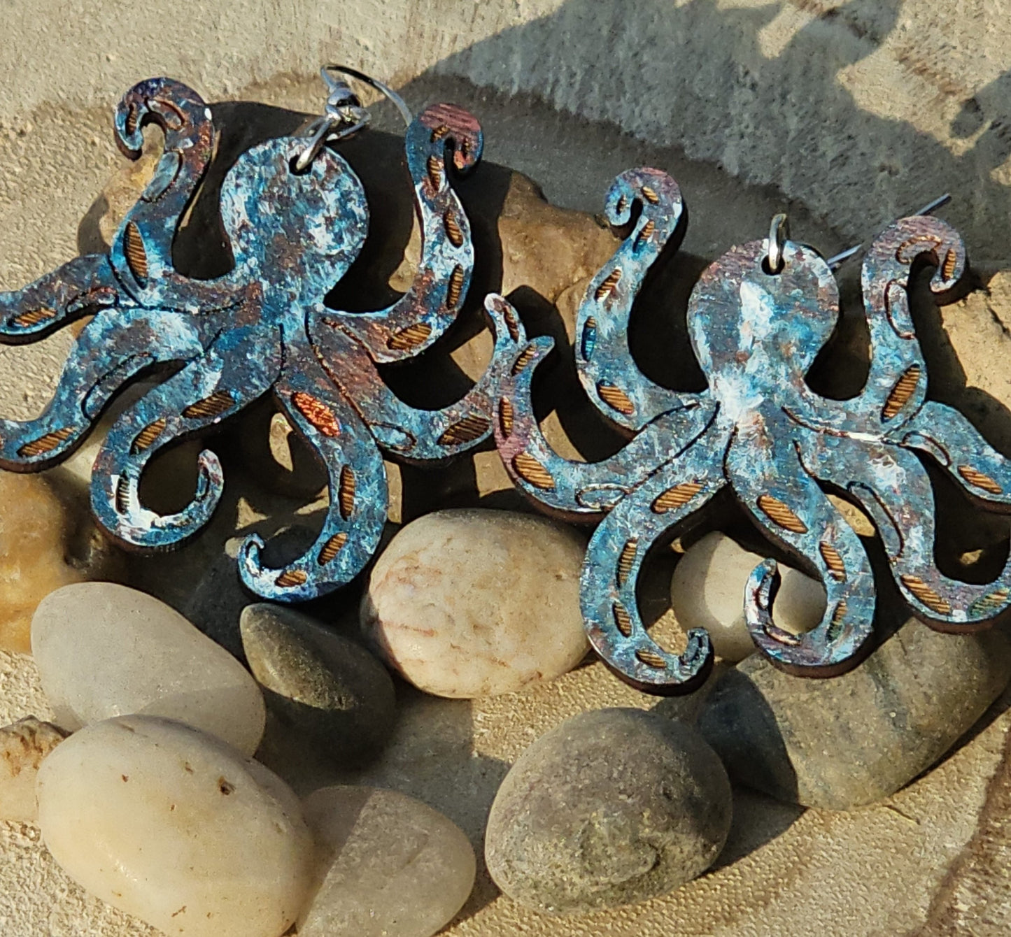 Metallic looking octopus-shaped earrings on pebbles