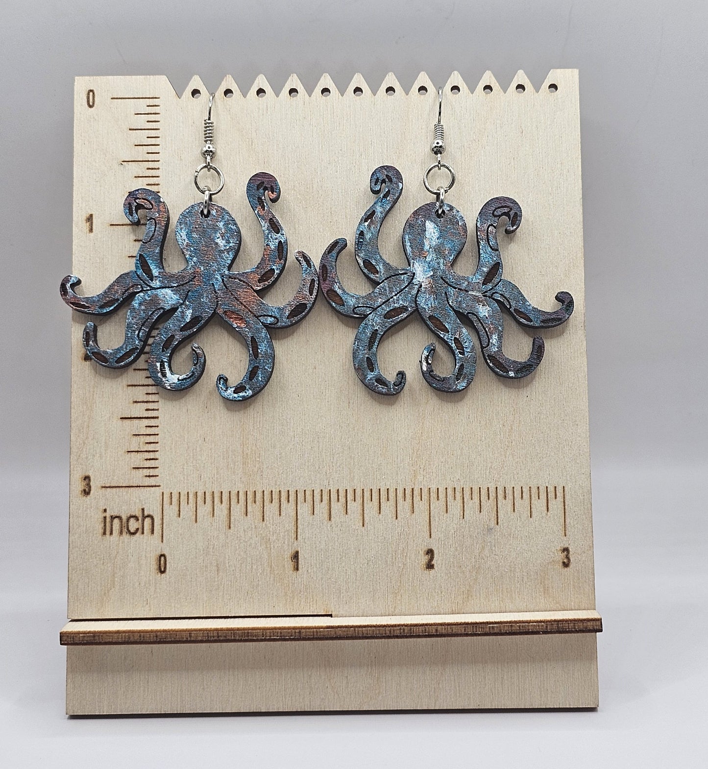 Octopus-shaped earrings on a wooden stand with a ruler for scale.