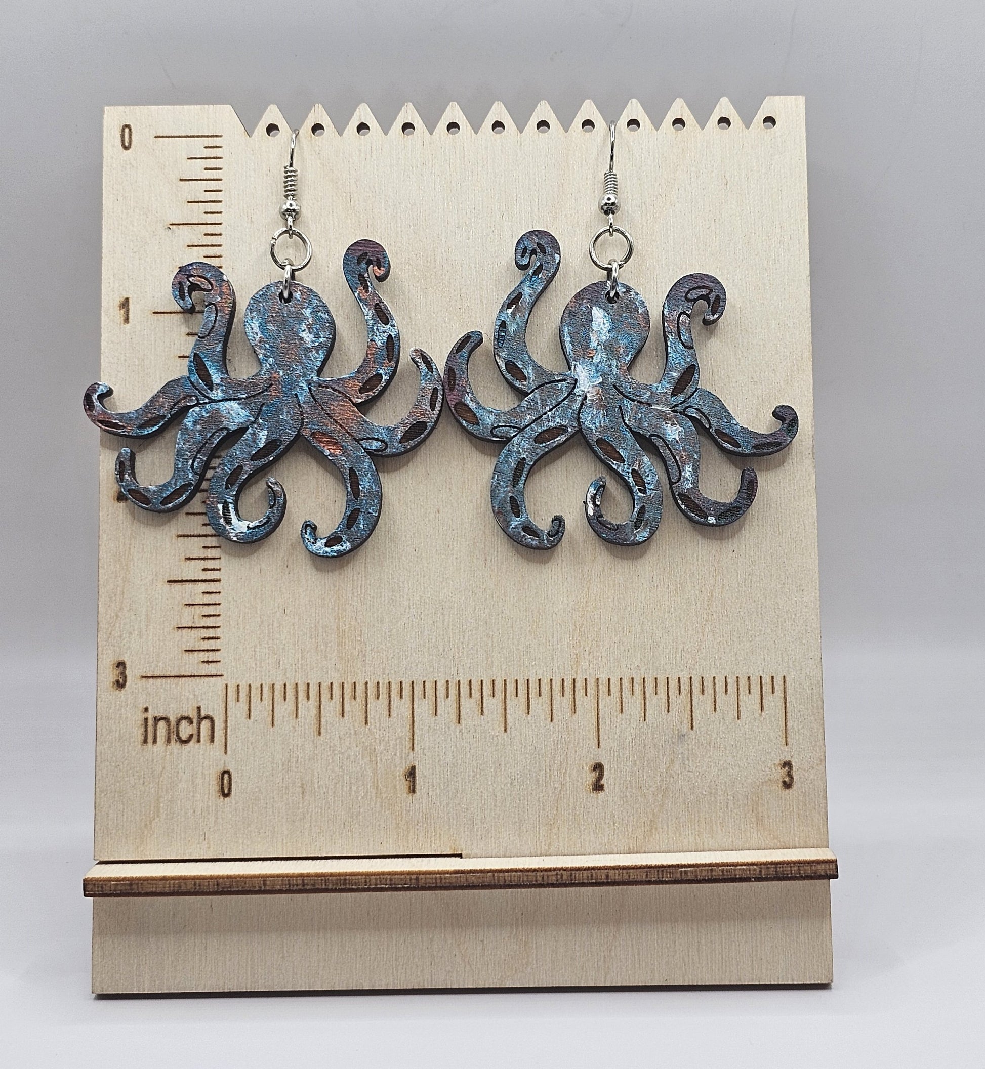 Octopus-shaped earrings on a wooden stand with a ruler for scale.