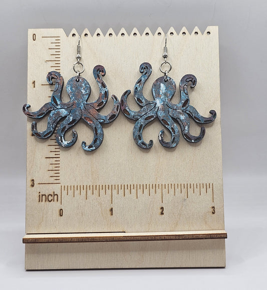 Octopus-shaped earrings on a wooden stand with a ruler for scale.