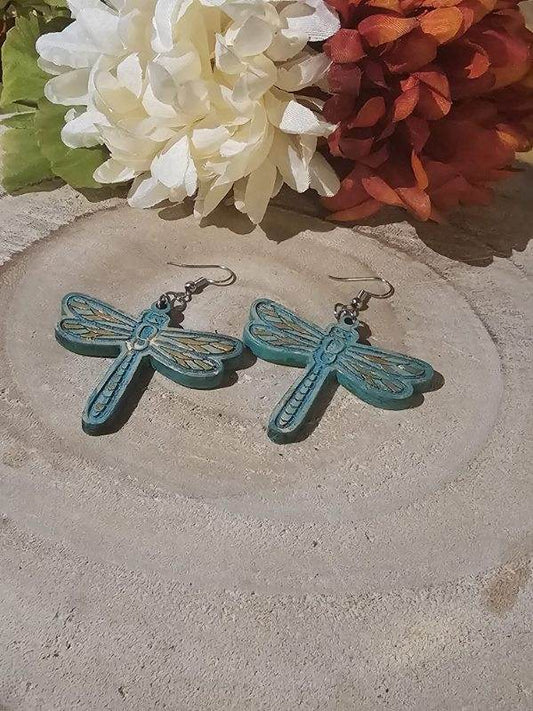 Dragonfly-shaped earrings on a stone surface with flowers in the background
