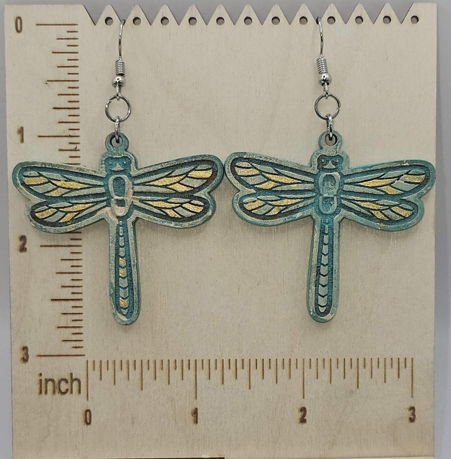 Dragonfly-shaped earrings on a wooden surface with a ruler for scale.