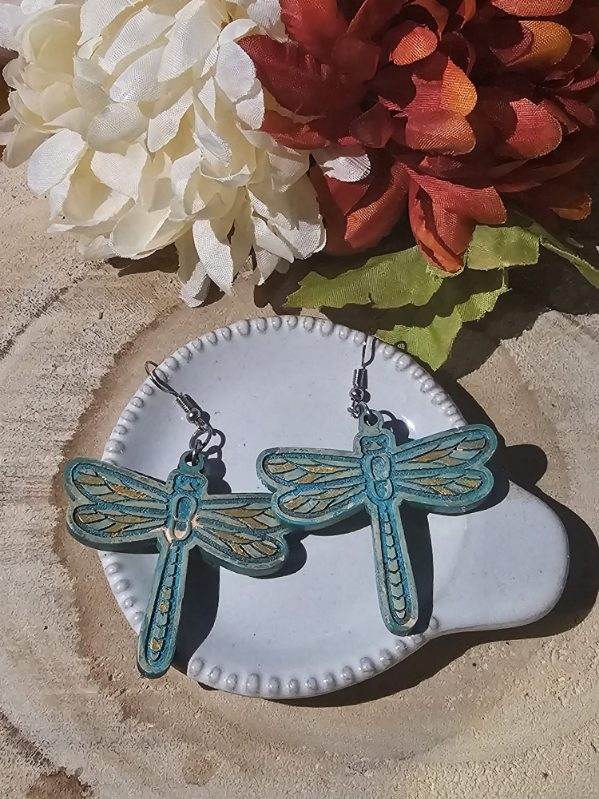 Dragonfly-shaped earrings on a white dish with flowers in the background