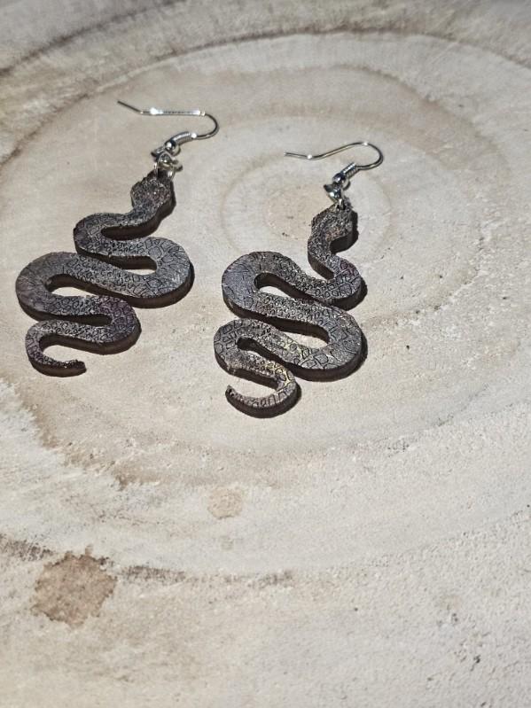 Snake-shaped earrings on a textured wood surface