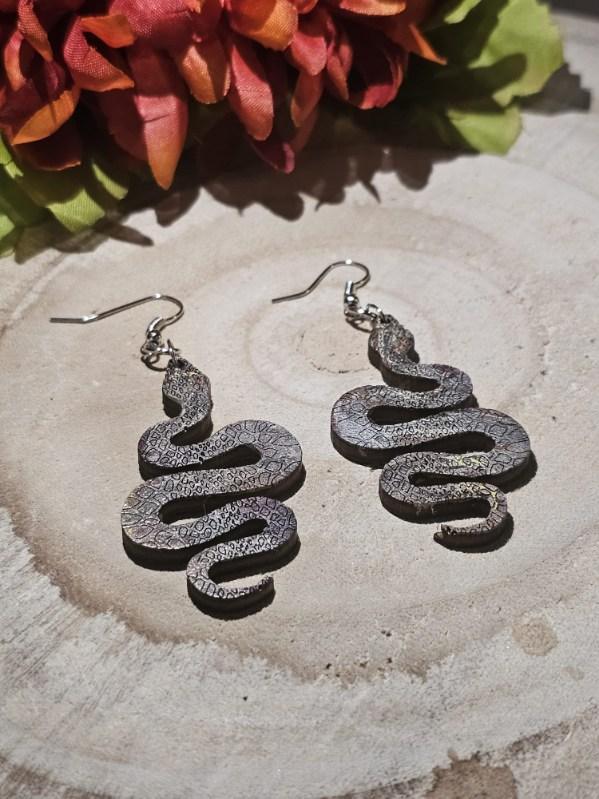 Serpentine earrings on a wooden surface with flowers in the background