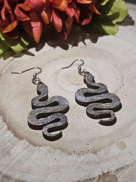 Serpentine earrings on a wooden surface with flowers in the background