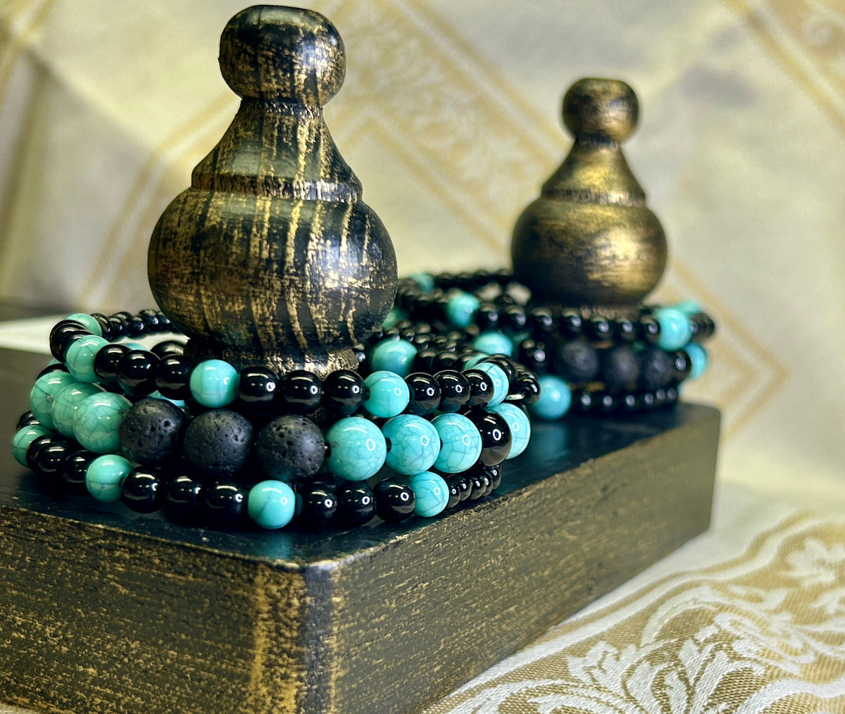 Set of black and turquoise beaded aromatherapy bracelets on a decorative stand with ornate background