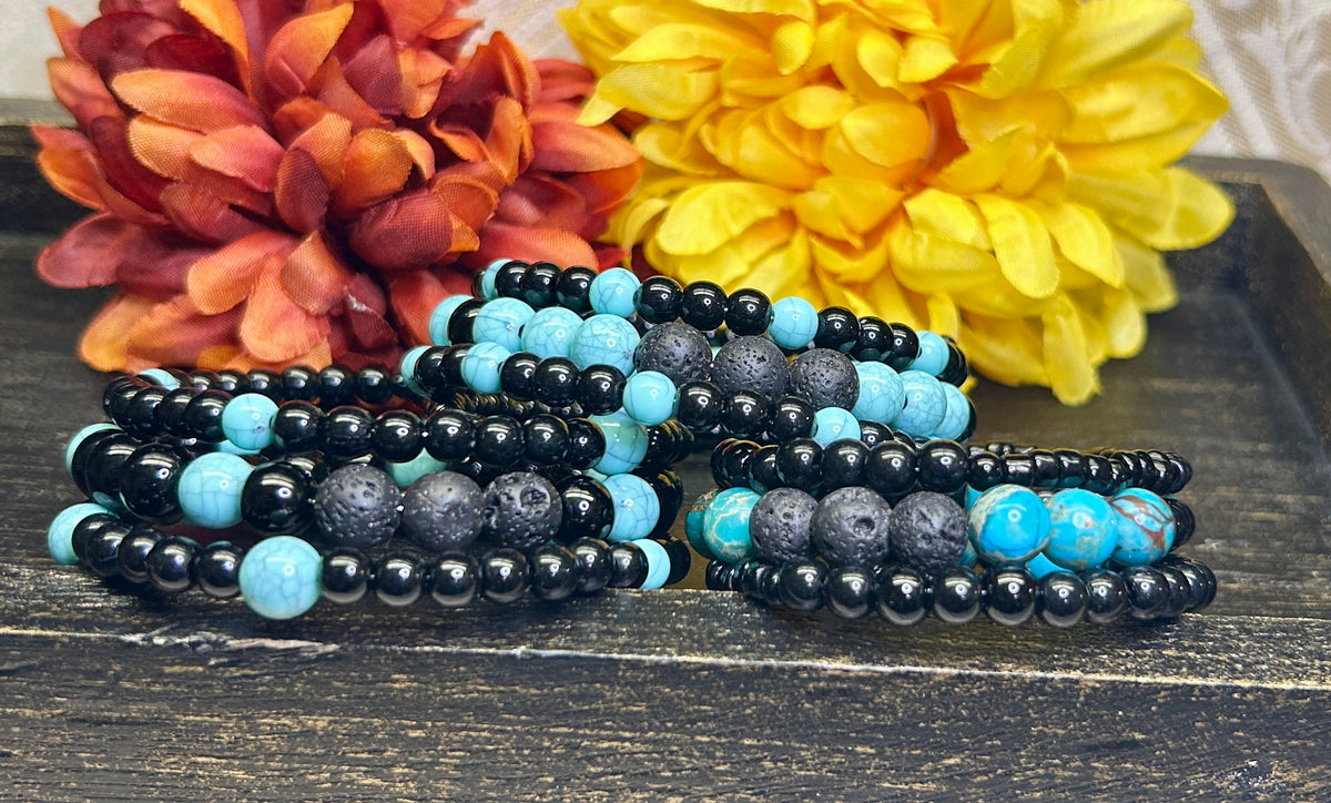 Three black and turquoise blue beaded aromatherapy bracelets on a wooden surface with flowers in the background.