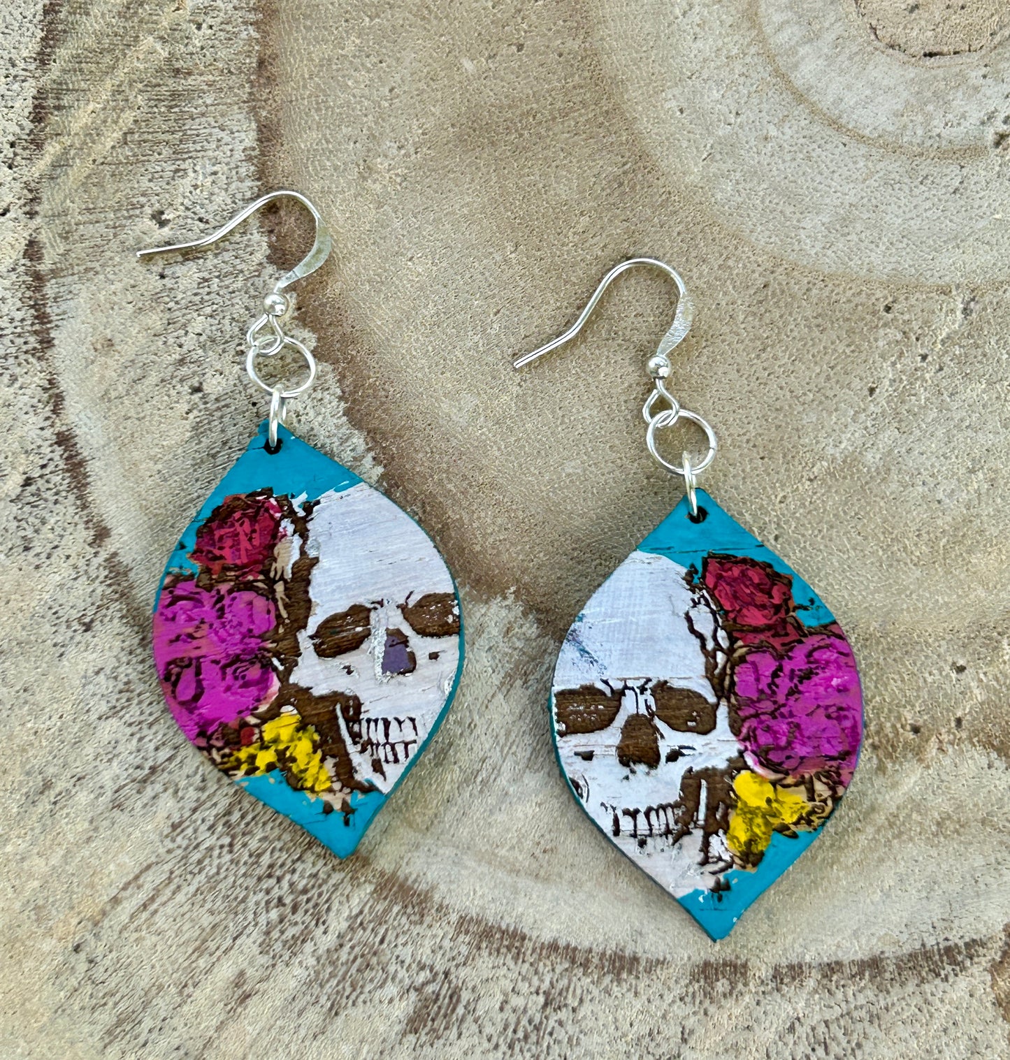 Pair of earrings with skull and floral design on a textured surface