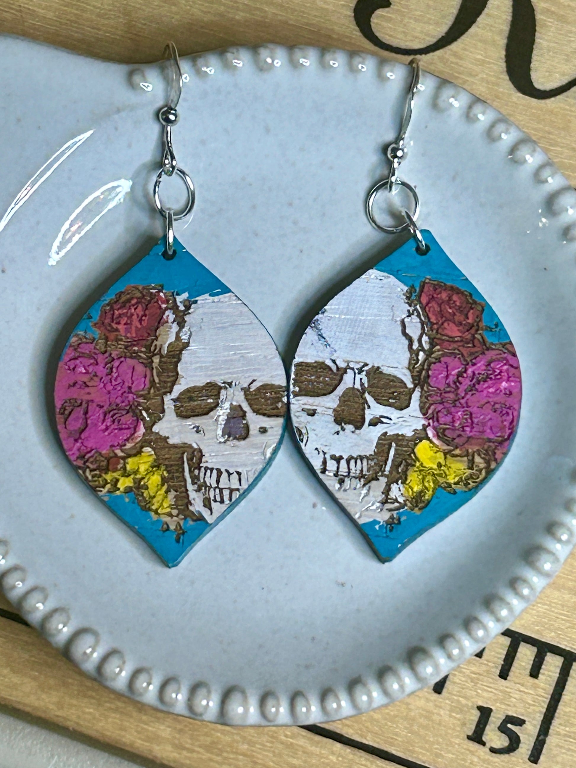 Pair of teardrop earrings with skulls and flowers on a white dish.