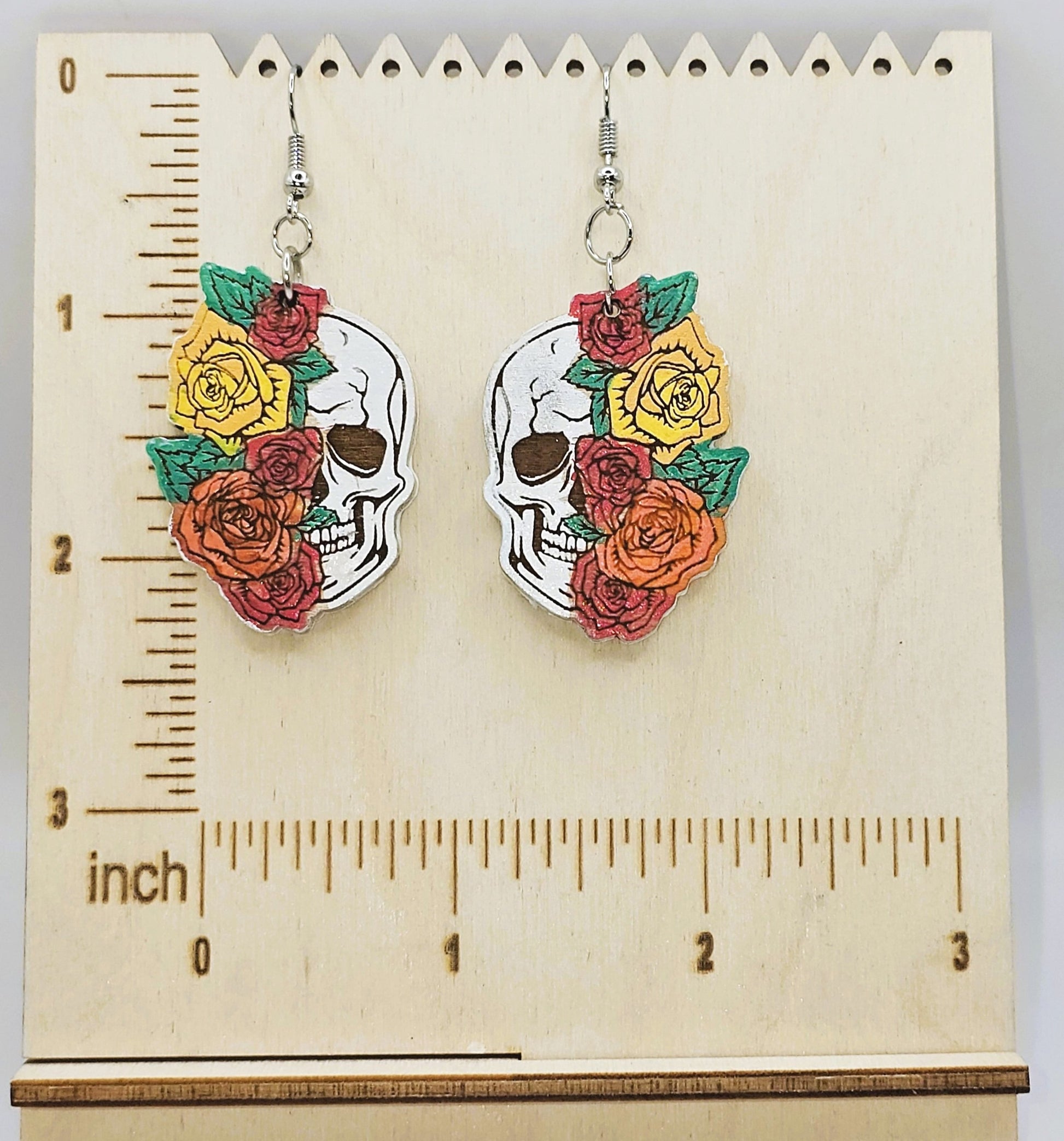 Skull and floral earrings on a wooden ruler for scale
